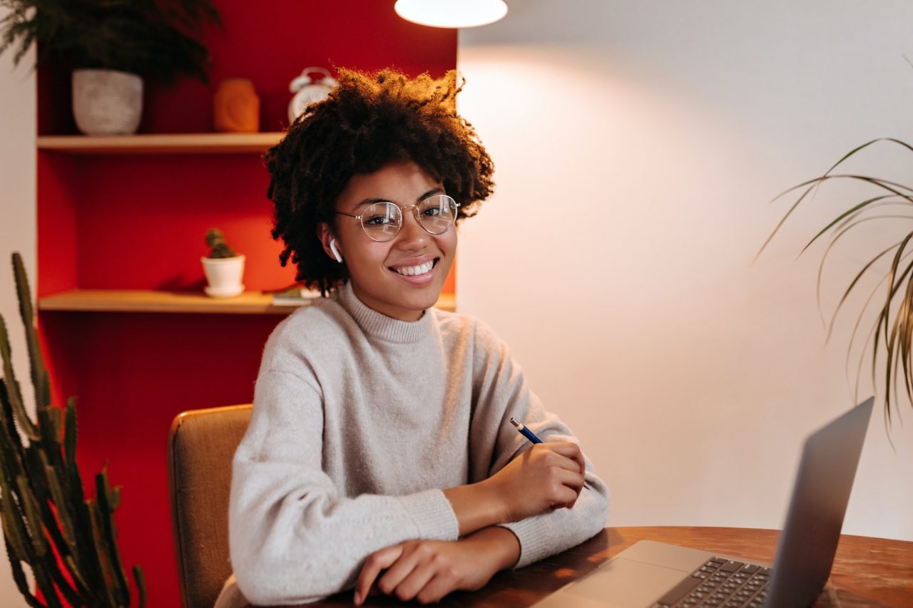 Positive Woman In Cashmere Sweater With Sweet Smile Looks At Camera And Poses In Workplace With Lap.jpg - Brasil CPF